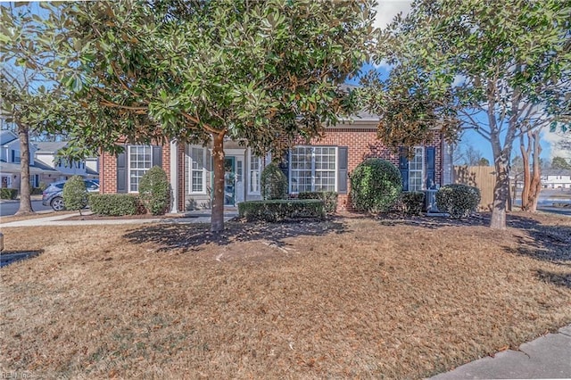 view of property hidden behind natural elements with fence, a front lawn, and brick siding