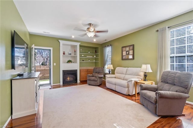 living area with a fireplace with flush hearth, ceiling fan, wood finished floors, and baseboards