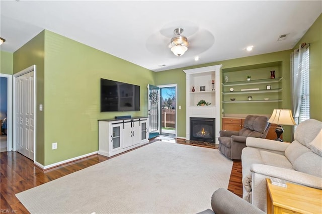 living room featuring dark wood-type flooring, a fireplace with flush hearth, a ceiling fan, and baseboards