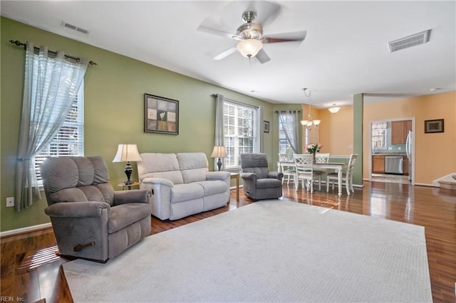 living area with ceiling fan with notable chandelier, dark wood finished floors, visible vents, and baseboards