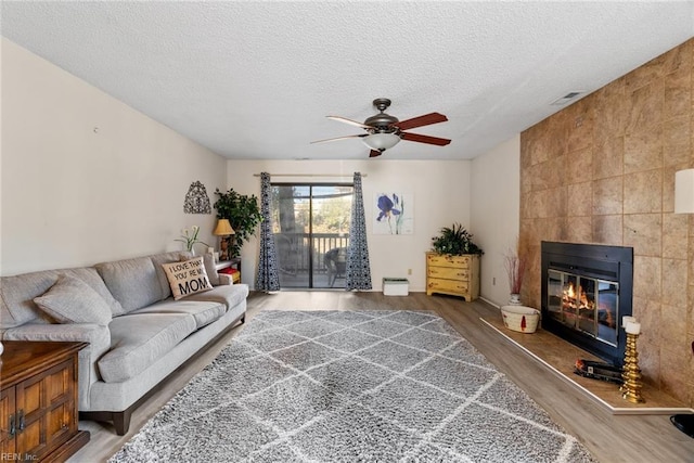 living area featuring a ceiling fan, a tile fireplace, wood finished floors, a textured ceiling, and tile walls