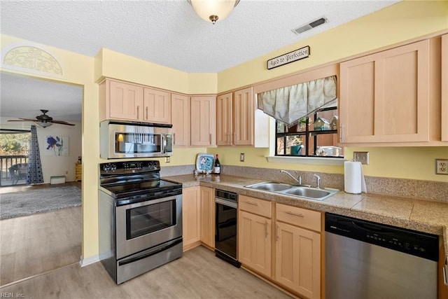 kitchen with tile countertops, stainless steel appliances, a sink, visible vents, and light brown cabinetry