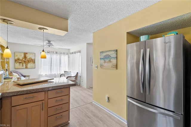 kitchen with tile countertops, a textured ceiling, light wood-type flooring, freestanding refrigerator, and pendant lighting