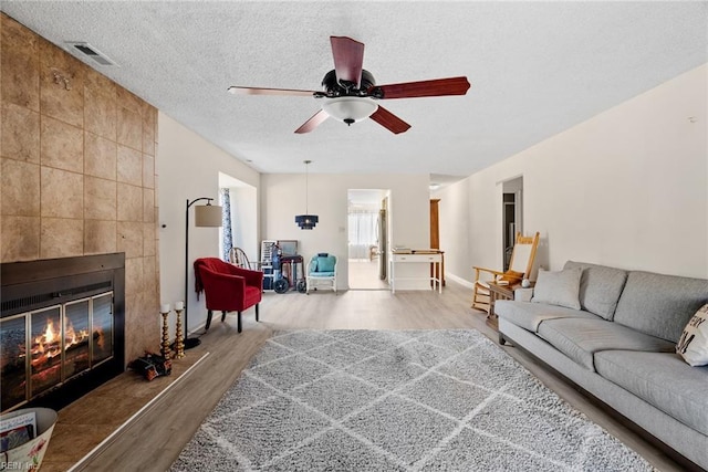 living room with a textured ceiling, ceiling fan, a fireplace, wood finished floors, and visible vents