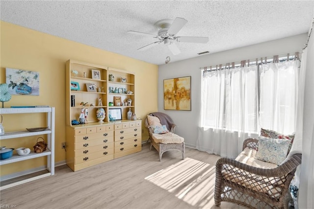 sitting room featuring a textured ceiling, ceiling fan, visible vents, baseboards, and light wood-style floors