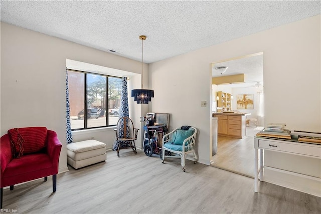 living area with a textured ceiling, light wood-type flooring, and visible vents