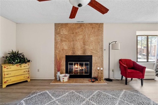 sitting room featuring a textured ceiling, wood finished floors, visible vents, a ceiling fan, and a tiled fireplace