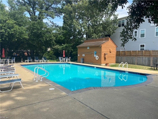 pool with a patio area, fence, and an outdoor structure