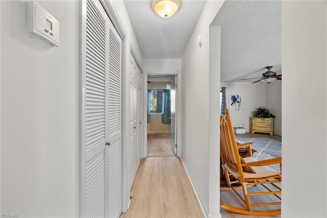 corridor featuring light wood-style floors, baseboards, and a textured ceiling