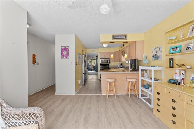 kitchen featuring a textured ceiling, a peninsula, appliances with stainless steel finishes, light wood finished floors, and a kitchen bar