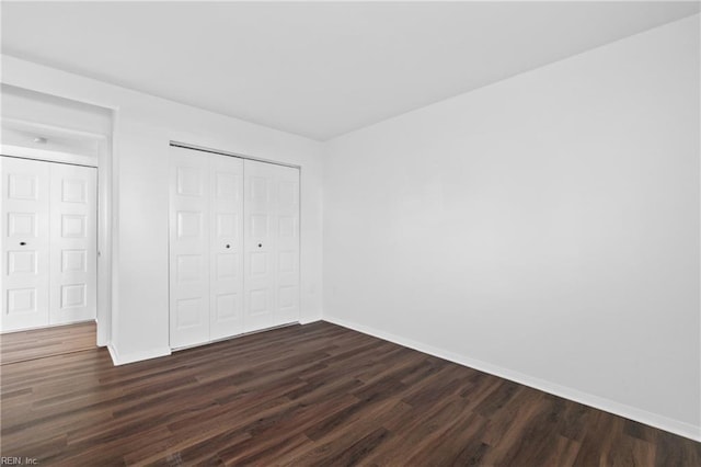 unfurnished bedroom with a closet, baseboards, and dark wood-style flooring