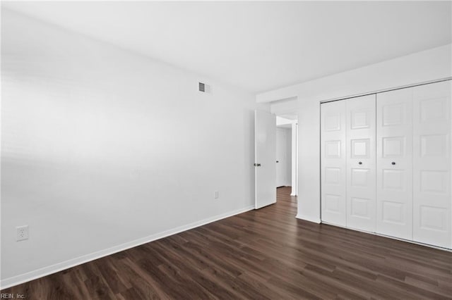 unfurnished bedroom with a closet, dark wood finished floors, visible vents, and baseboards