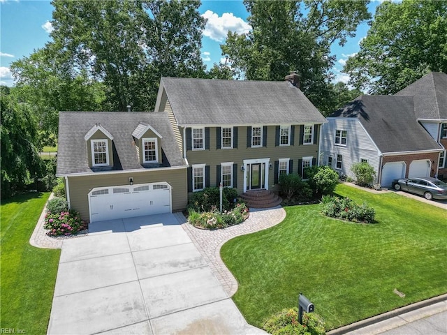 colonial-style house featuring an attached garage, a shingled roof, concrete driveway, and a front yard