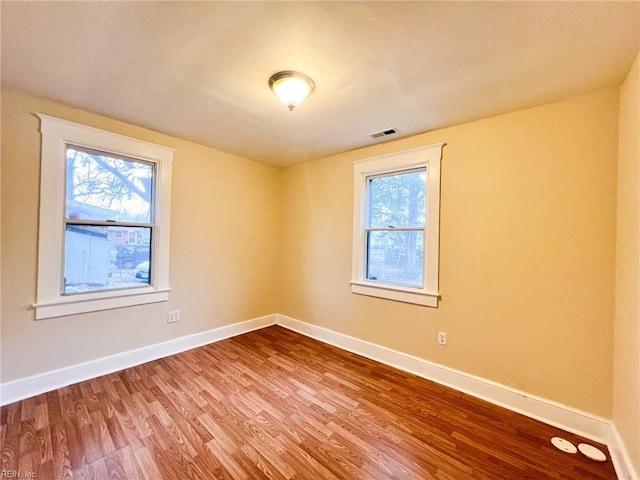 spare room featuring a wealth of natural light, wood finished floors, visible vents, and baseboards
