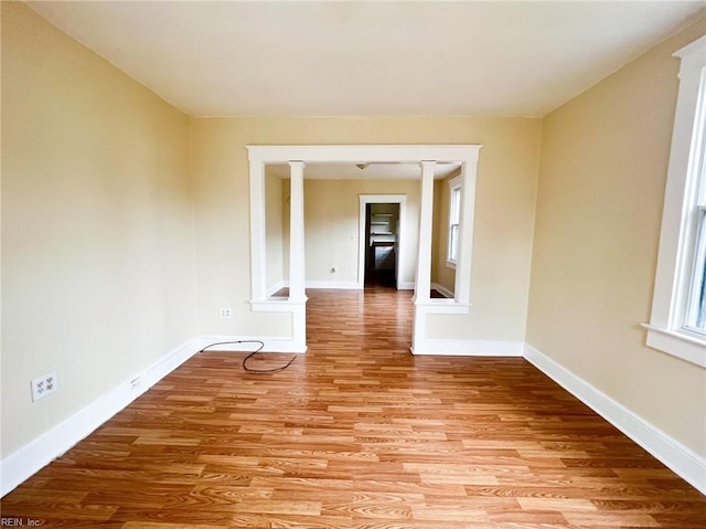 unfurnished room with baseboards, light wood-style floors, and ornate columns