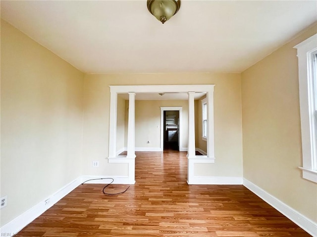 empty room featuring ornate columns, light wood finished floors, and baseboards