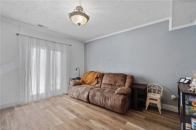 living area featuring a textured ceiling, visible vents, baseboards, light wood-style floors, and ornamental molding