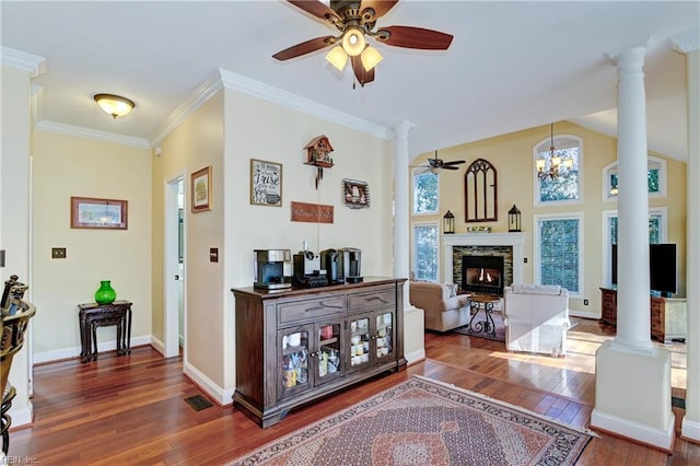 interior space with ceiling fan, a stone fireplace, ornamental molding, dark wood-style floors, and decorative columns