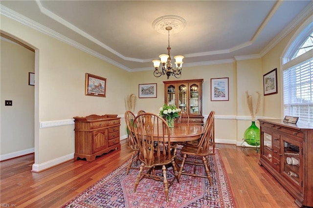 dining area featuring a chandelier, arched walkways, light wood-style flooring, baseboards, and a tray ceiling