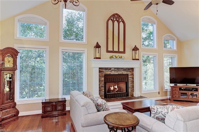 living area featuring a fireplace, ceiling fan, wood finished floors, high vaulted ceiling, and baseboards