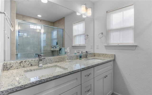 bathroom featuring double vanity, a stall shower, a sink, and a textured wall