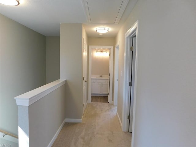 corridor with attic access, baseboards, light colored carpet, an upstairs landing, and a sink