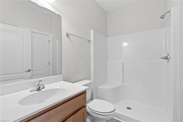 bathroom featuring a textured wall, vanity, toilet, and walk in shower