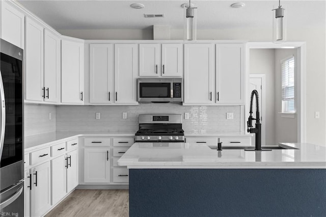 kitchen with stainless steel appliances, white cabinetry, light wood-style flooring, and decorative backsplash