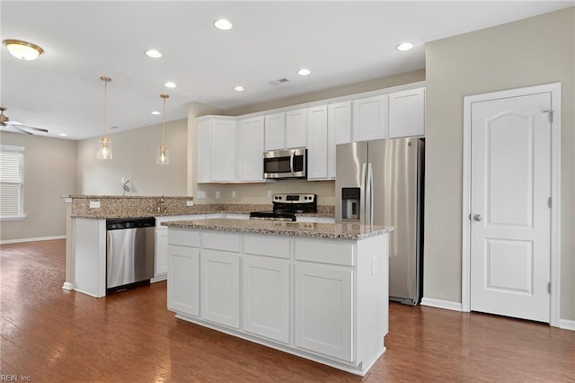 kitchen featuring light stone counters, stainless steel appliances, a kitchen island, white cabinets, and hanging light fixtures