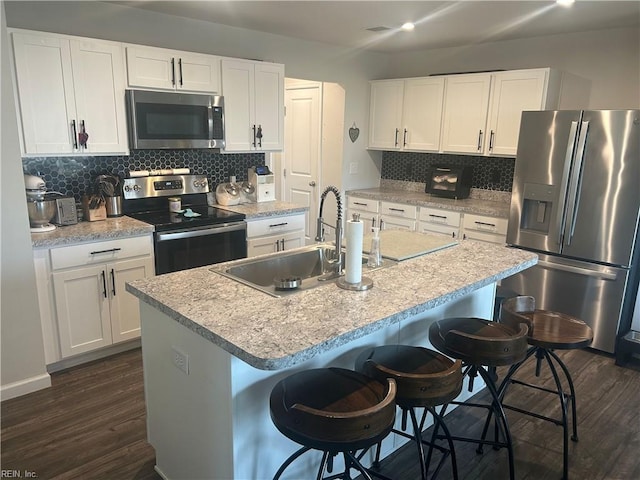 kitchen with dark wood-style flooring, a sink, stainless steel appliances, white cabinetry, and a kitchen breakfast bar