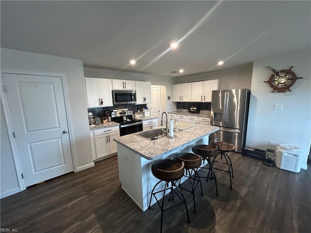 kitchen with a sink, a center island with sink, appliances with stainless steel finishes, a kitchen breakfast bar, and dark wood-style flooring