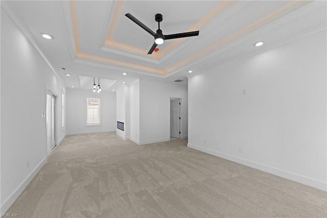 unfurnished living room featuring a tray ceiling, ornamental molding, light carpet, ceiling fan, and baseboards