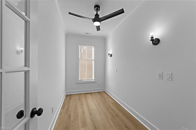 empty room with crown molding, light wood finished floors, visible vents, ceiling fan, and baseboards