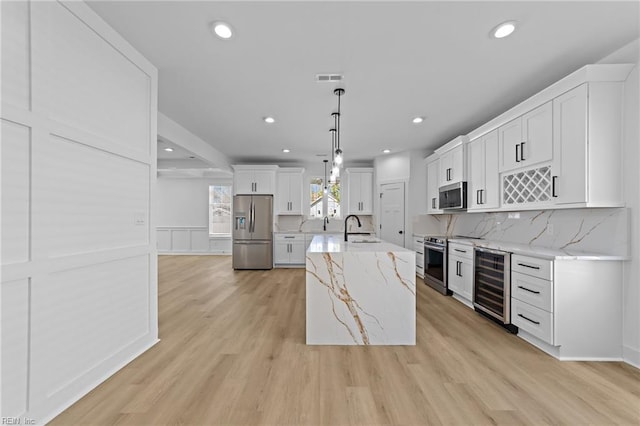 kitchen featuring wine cooler, decorative light fixtures, appliances with stainless steel finishes, white cabinetry, and a sink