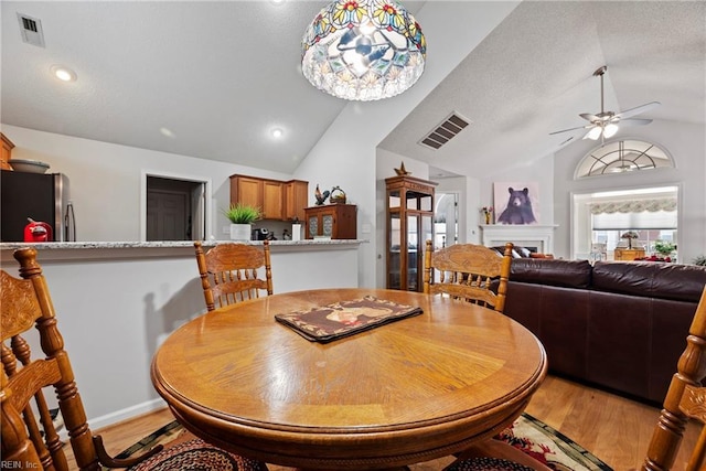 dining area featuring lofted ceiling, light wood finished floors, a fireplace, and visible vents