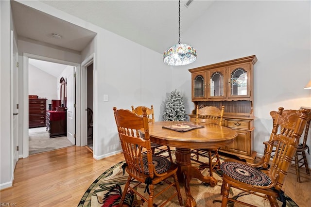 dining room featuring lofted ceiling, light wood-type flooring, and baseboards