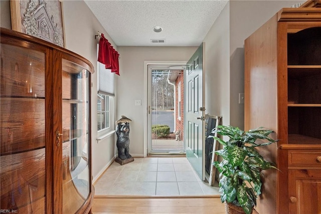 doorway with baseboards, visible vents, a textured ceiling, french doors, and light tile patterned flooring