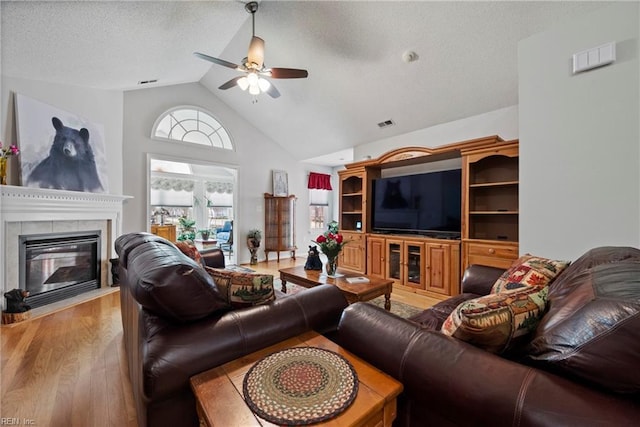 living room featuring visible vents, a ceiling fan, a textured ceiling, light wood-type flooring, and a tile fireplace