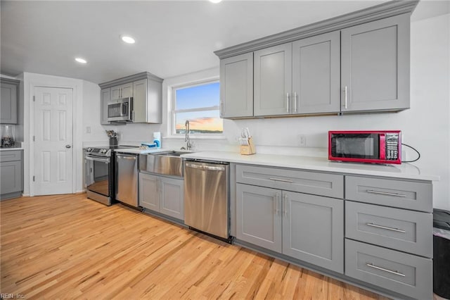 kitchen featuring stainless steel appliances, a sink, light wood-style floors, light countertops, and gray cabinets