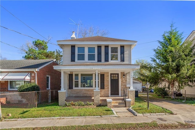 traditional style home with covered porch, fence, and a front yard