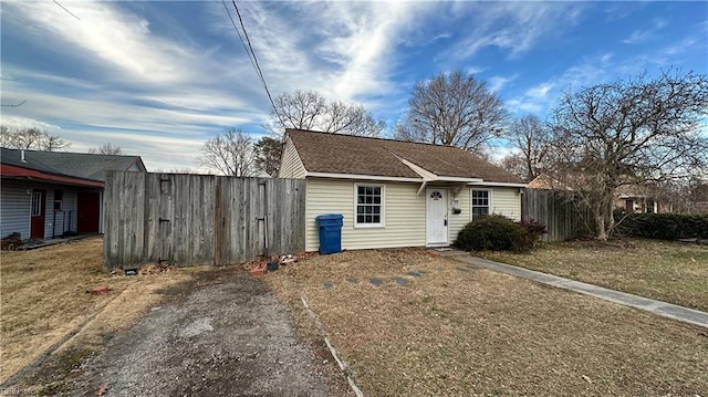 view of front of home featuring driveway, roof with shingles, a gate, fence, and a front lawn