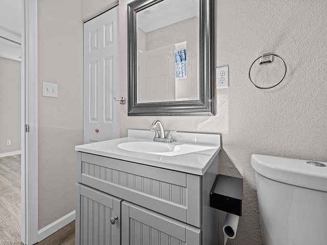 half bath featuring a textured wall, vanity, and wood finished floors