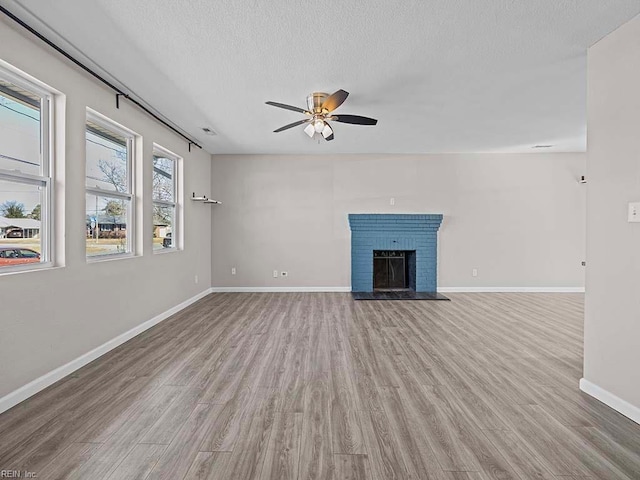 unfurnished living room featuring baseboards, a ceiling fan, wood finished floors, a textured ceiling, and a fireplace