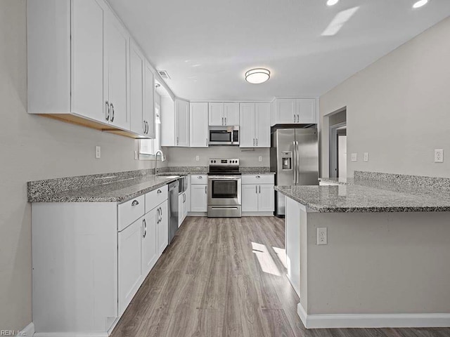 kitchen with a peninsula, light stone countertops, stainless steel appliances, white cabinetry, and a sink