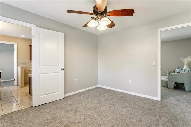 unfurnished bedroom with a walk in closet, light colored carpet, light tile patterned flooring, ceiling fan, and baseboards