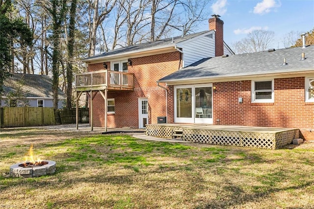 back of house with brick siding, a lawn, fence, a fire pit, and a wooden deck