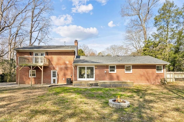 rear view of property with brick siding, a chimney, a lawn, fence, and a fire pit