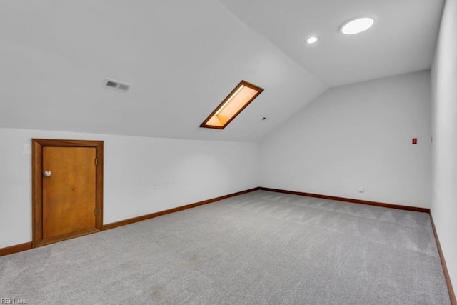 additional living space featuring light carpet, vaulted ceiling with skylight, visible vents, and baseboards