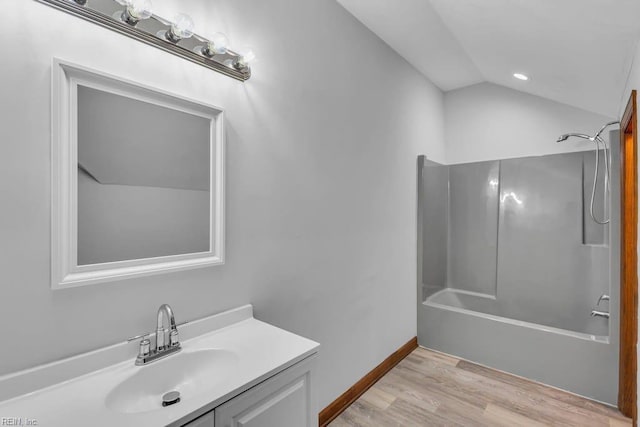 bathroom featuring bathing tub / shower combination, lofted ceiling, vanity, wood finished floors, and baseboards