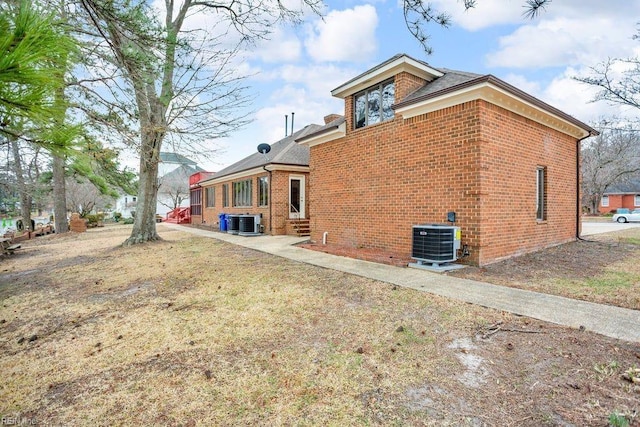 back of house with entry steps, central AC, brick siding, and a lawn